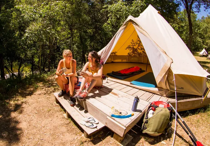 Deux amies devant une tente cosy sur une aire de bivouac